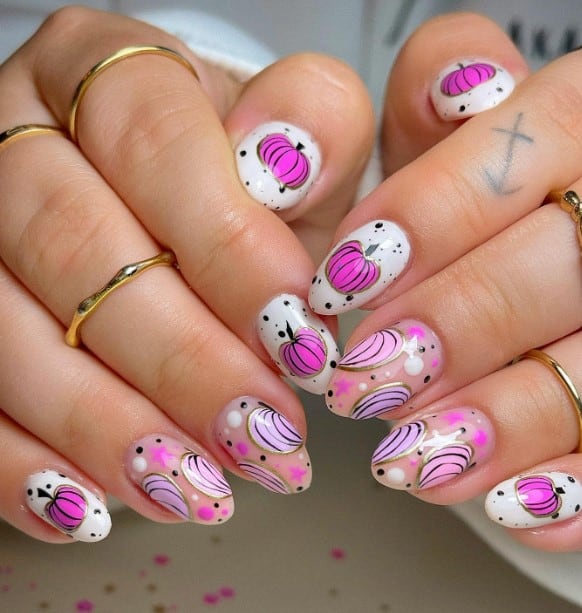 A closeup of a woman's fingernails with a white and nude nail polish base that has pink pumpkins with black speckles on a white base