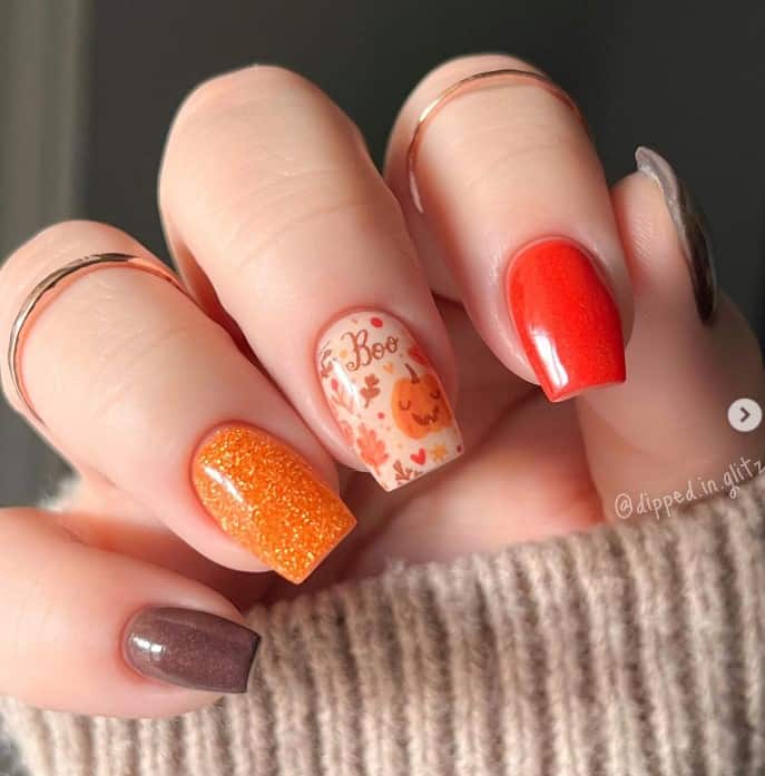 A closeup of a woman's fingernails with a glittery orange and brown nail polish that has smiling pumpkins, hearts, leaves, dots, and bright, classic fall colors