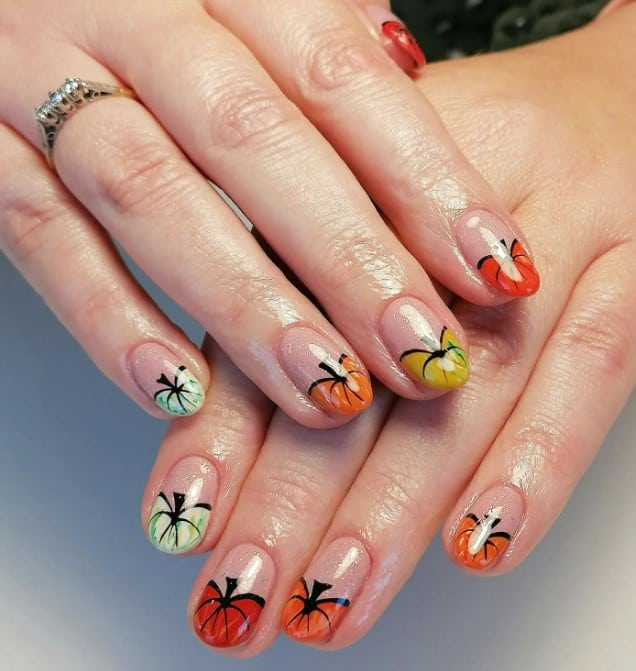 A closeup of a woman's fingernails with a glittery nude nail polish base that has pumpkin tips in various fall-themed colors