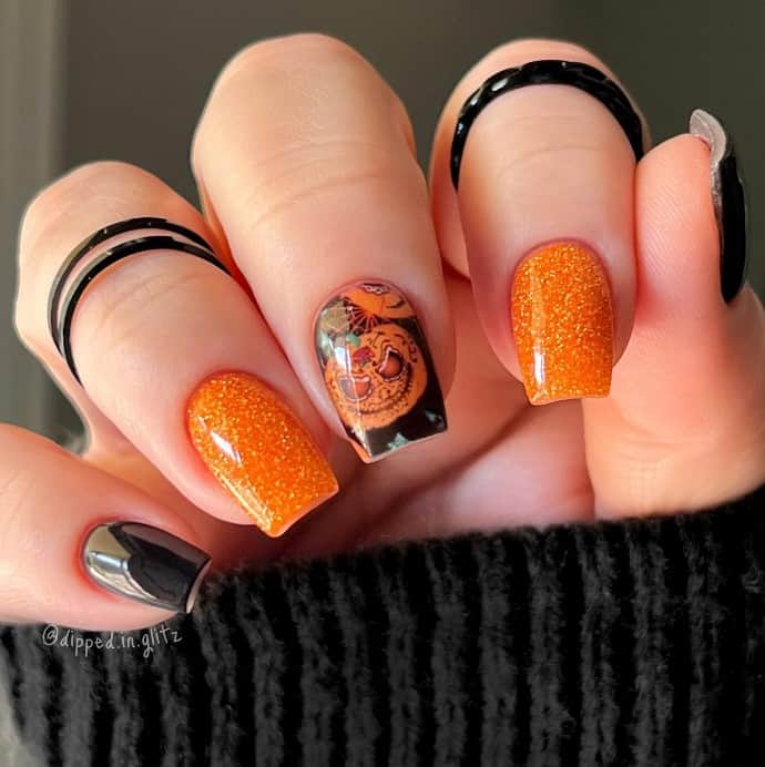 A closeup of a woman's fingernails with a glittery orange and black colors that has Halloween pumpkin nails on select nails