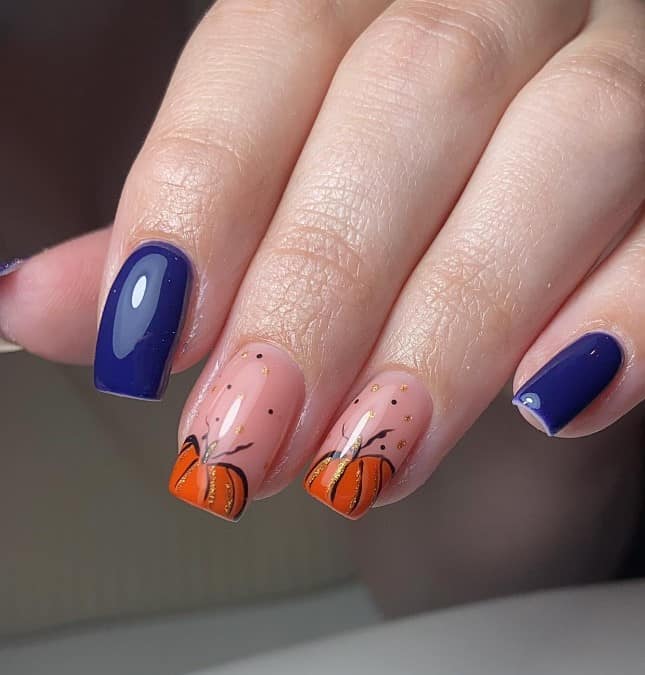 A closeup of a woman's fingernails with a solid blue and nude nail polish base that has orange pumpkins on select nails 