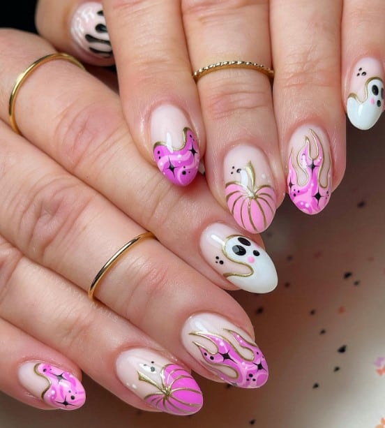 A closeup of a woman's fingernails with a white nail polish base that has French tips with different designs in pink, purple, black, and white outlined with gold and ghosts, pumpkins, flames, drips, and marbly blobs