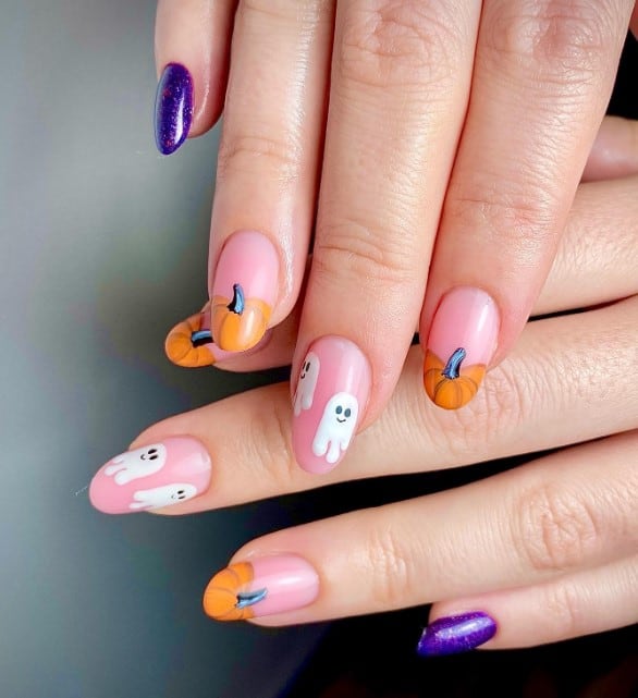 A woman's fingernails with pink and purple nail polish that has pumpkins and ghosts nail designs on pink nails 