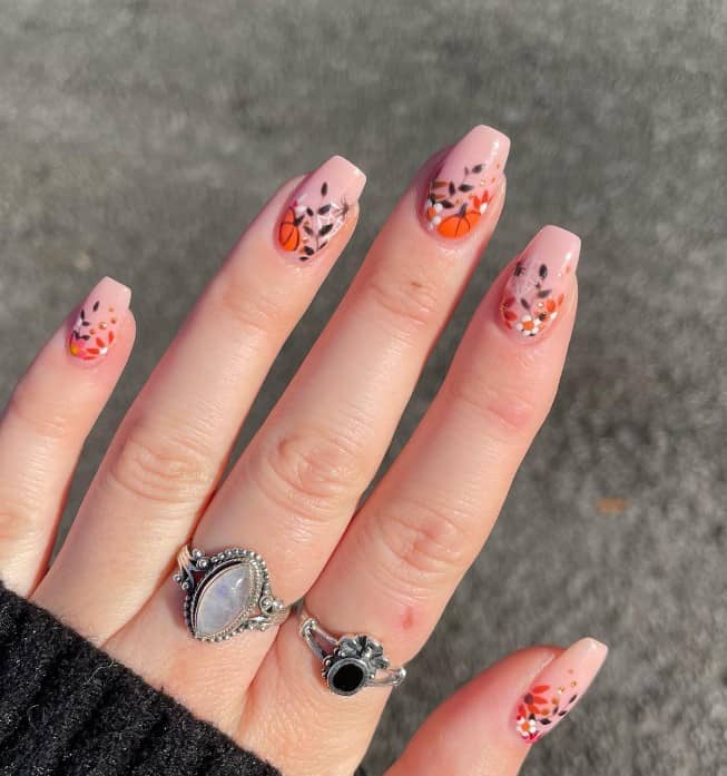 A woman's fingernails with a nude pink base that has pumpkins, florals, and black and white leaves