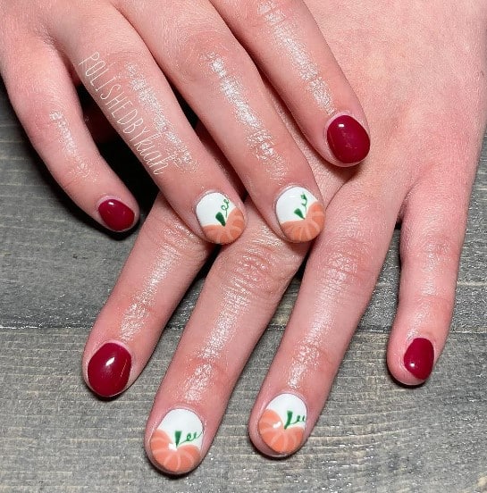 A woman's fingernails with a combination of maroon and white nail polish base that has brownish-orange pumpkins on white nails 