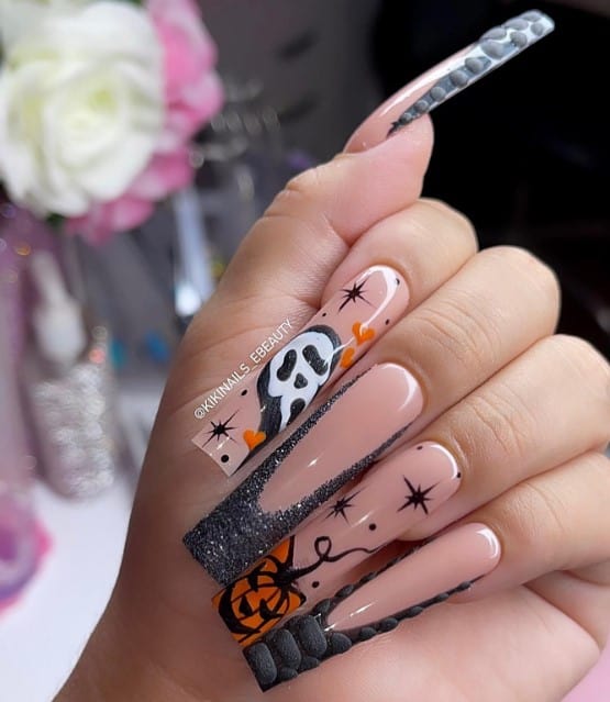 A woman's fingernails with a nude nail polish base that has 3D animal print and sparkly black beveled designs, a spooky ghoul, a mean-looking pumpkin, and sparkling stars