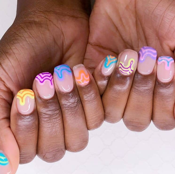A closeup of a woman's nails with nude nail polish that has pink and purple, blue and purple, orange and pink, and yellow and orange swirls 