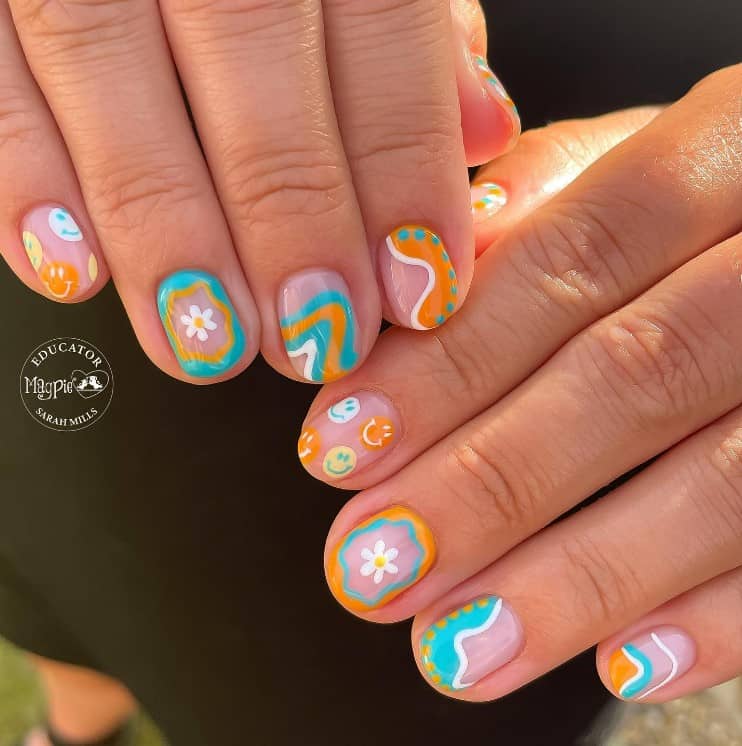 A closeup of a woman's clear nails with orange, turquoise, yellow, and white colors that has smileys, flowers, dots, and swirls nail designs