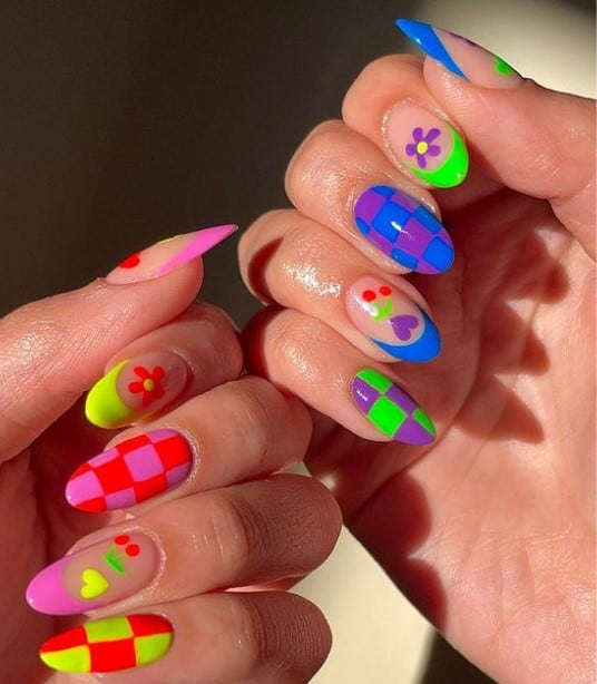A woman's nails with warm tones on the nails on one hand and cool tones on the other that has French tips and heart, checkered, floral, and cherry nail art