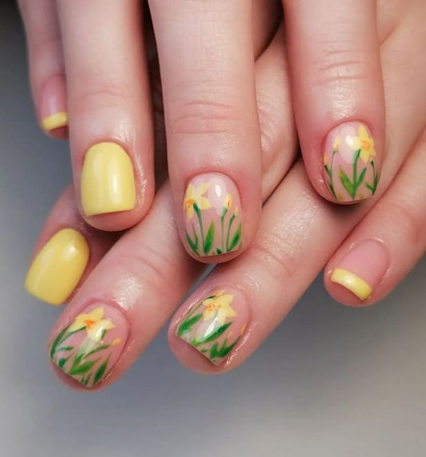 A closeup of a woman's nails with nude and yellow nail polish base that has daffodil accent nails on nude nails 