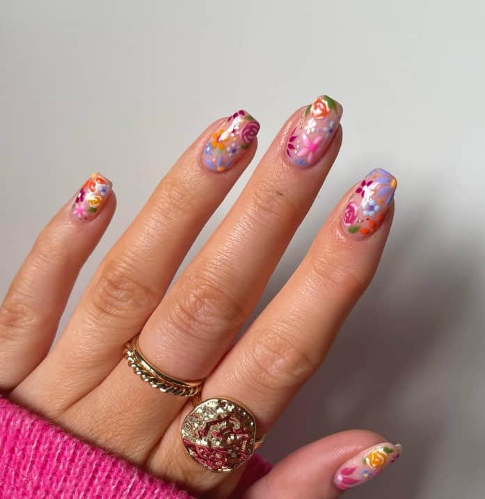 A woman's nude colored nails that has floral designs in multiple colors on each nail