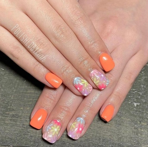 A woman's short nails with orange and nude nail polish base that has flowery patterns on nude nails 