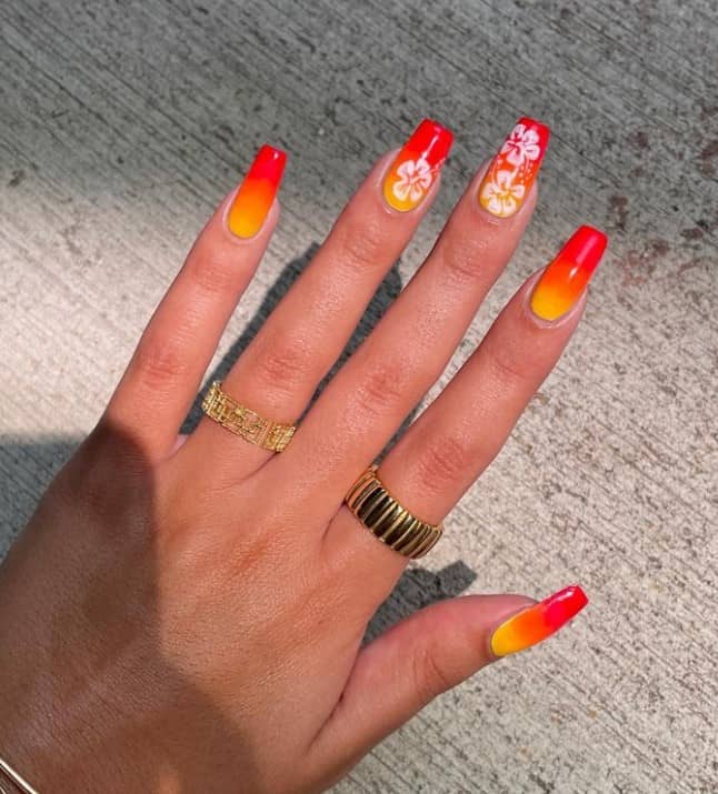 A woman's nails with an ombré orange-and-yellow base that has tropical flowers in white on select nails 