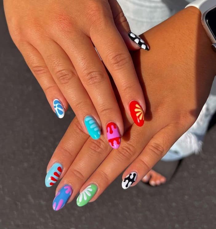 A woman's short nails with bright and colorful nail polish base that has drip designs and flower details 