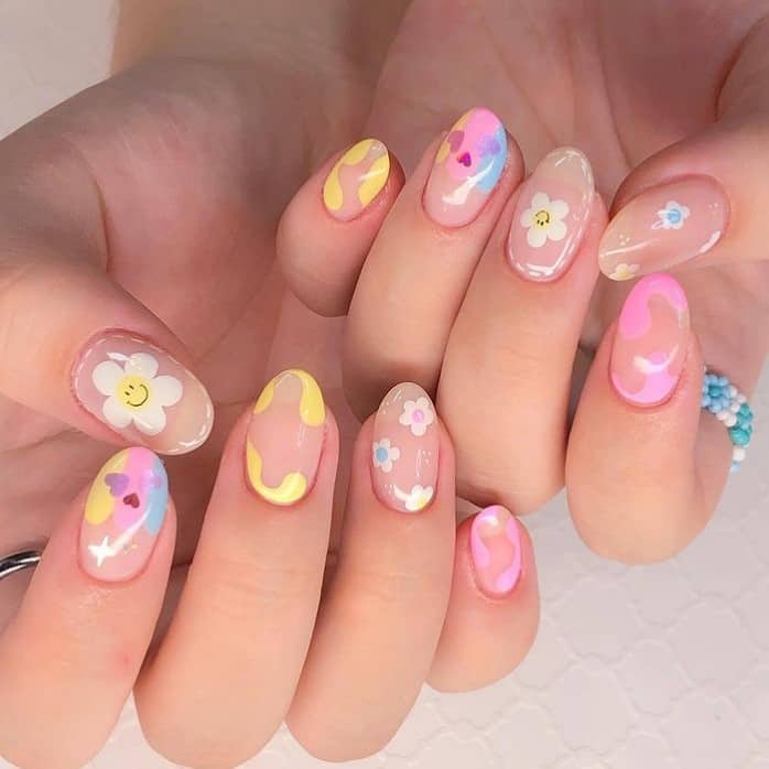 A closeup of a woman's nails with nude nail polish base that has different pastel colors with swirls, flowers, and smiley face designs