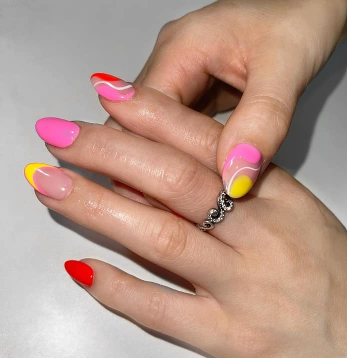 A woman's short nails with yellow, pink, red, and white manicure that has swirls, negative space nail art, and French tips