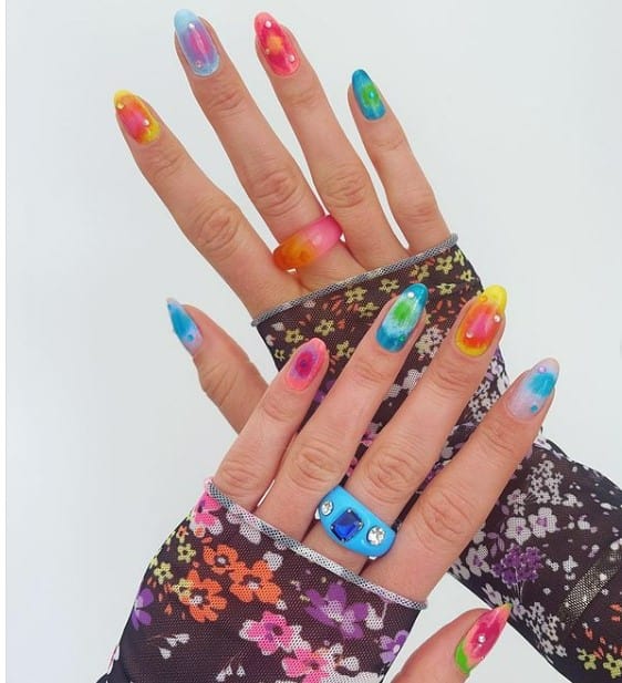 A woman's short nails with multicolored nail polish in an an airbrushed aura look that has jewels 