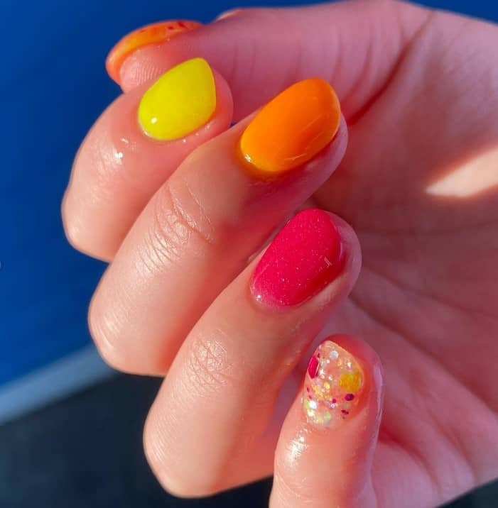 A closeup of a woman's short nails with neon nails in juicy colors that has a chunky glitter accent nail