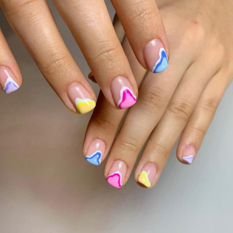 A woman's nails with nude nail polish that has lighter and darker pastel color combinations for the tips in a a spilled-paint look