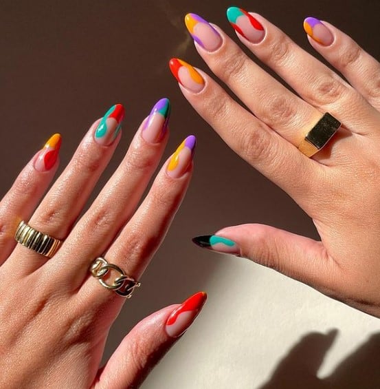 A woman's long nails with nude nail polish base that has French tips with swirls in orange, red, purple, and teal colors