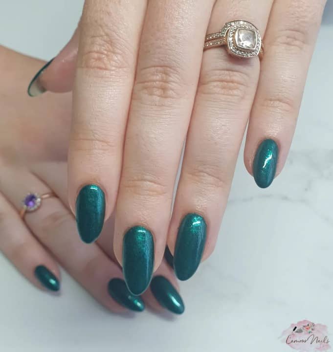 A closeup of a woman's long nails with a teal nail polish base in a glittery finish