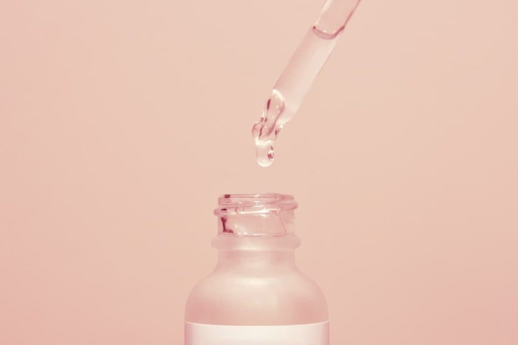 Face serum drop with bottle on a pink background