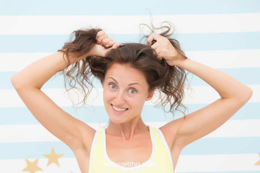 a woman wearing a tank top with 2a hair holding her hair with both hands happily