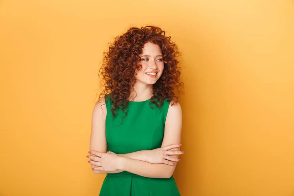 a young woman with bouncy and gorgeous curls looking fab at the camera with the bright orange background