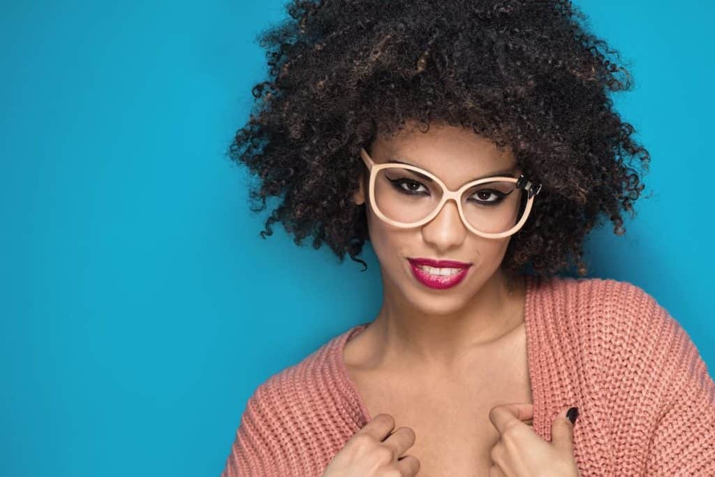 a woman wearing a pastel pink eyeglasses and wearing a cardigan is posing seriously at the camera