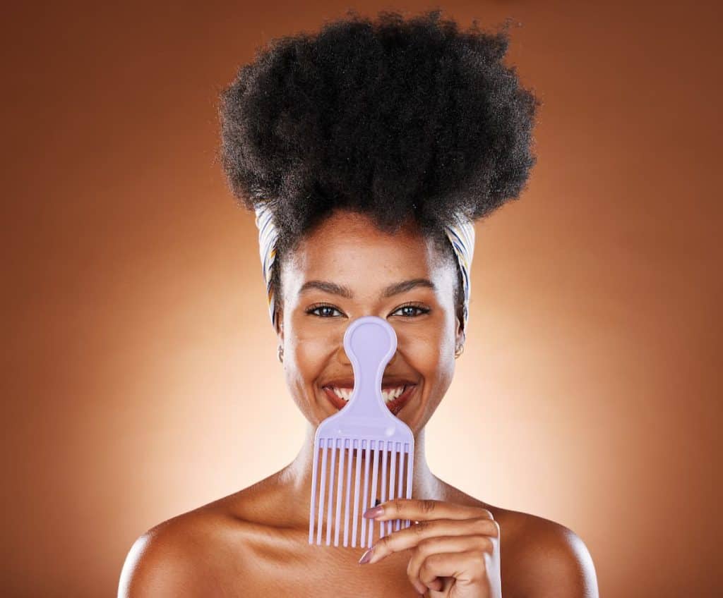 a beautiful black woman with 4c hair smiling at the camera while holding a comb
