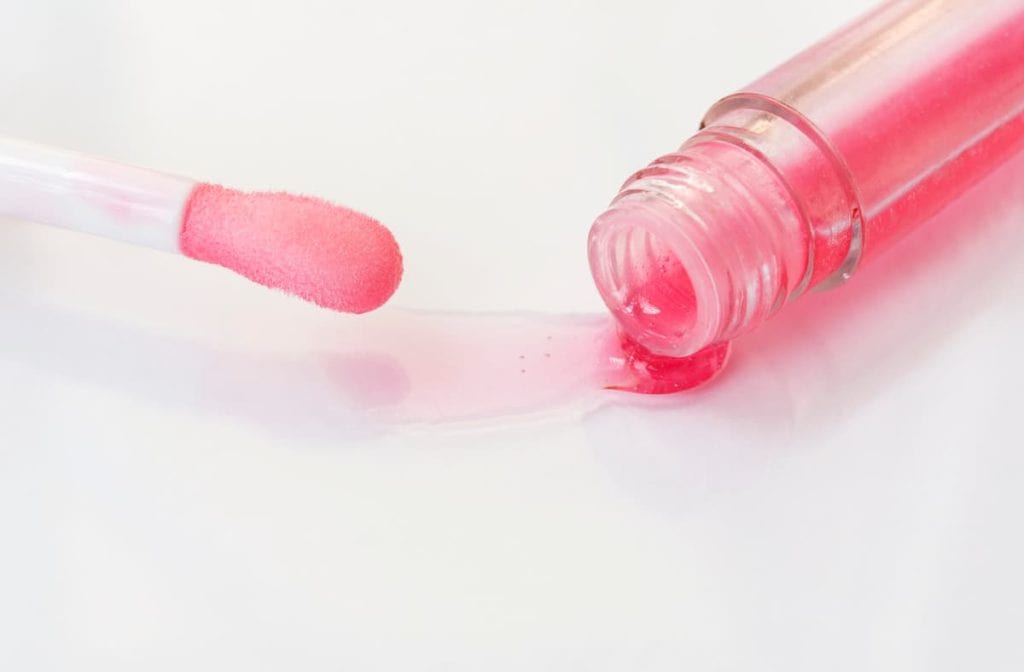 A pink lip oil is being poured into a bottle.