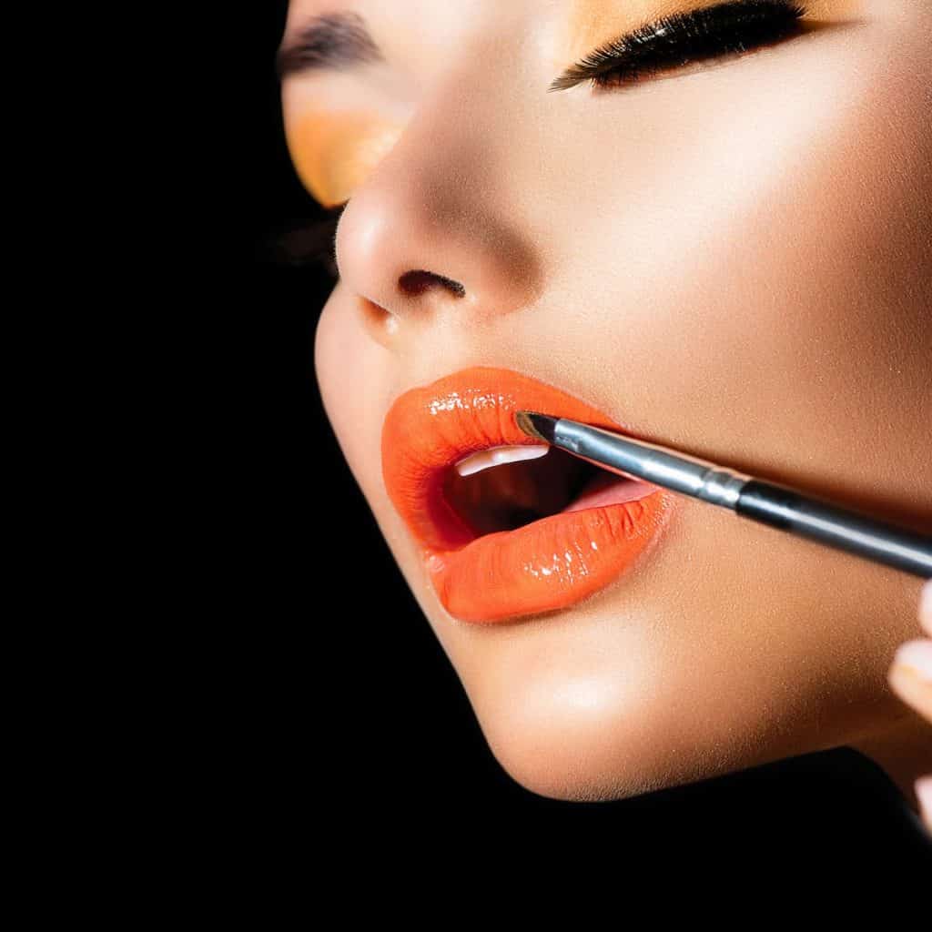 a close-up image of a woman with a full glam make up and using the best orange lipstick on her lips