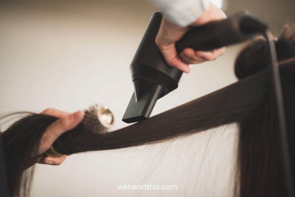a close-up image of a hairstylist using a blow dryer to straighten hair