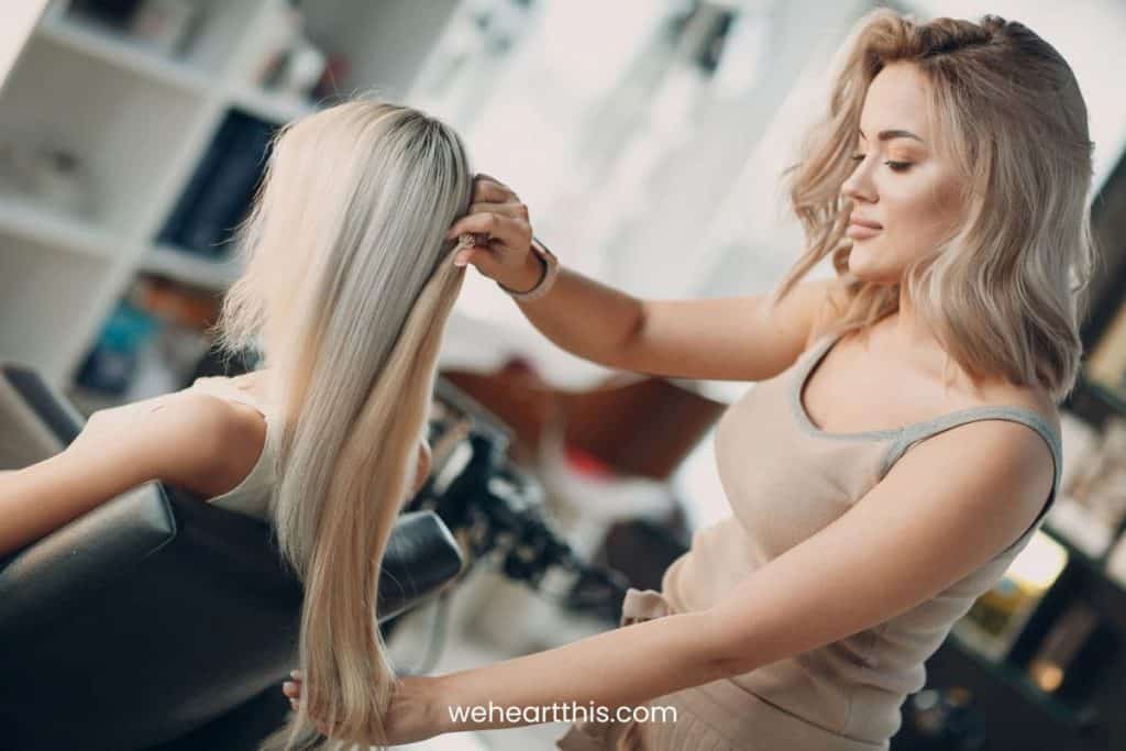 a hair stylist checking the hair extensions length to her client in the salon