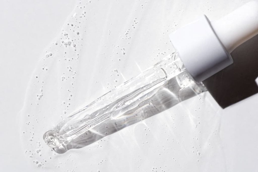A bottle with a drop of serum on a white surface.