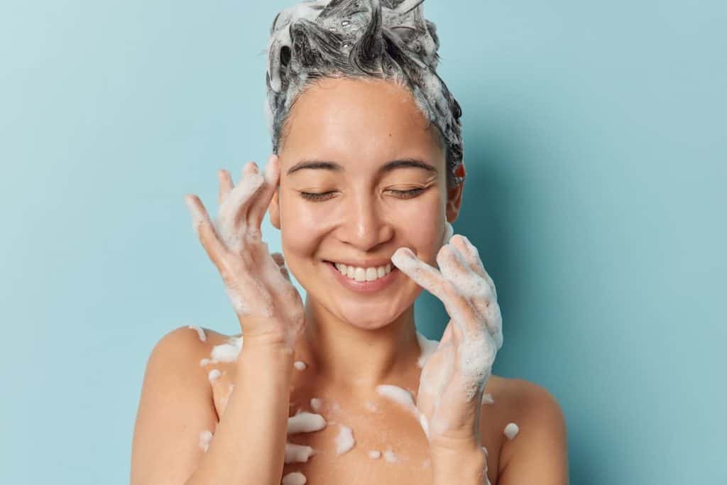 A woman is applying shampoo on her hair.