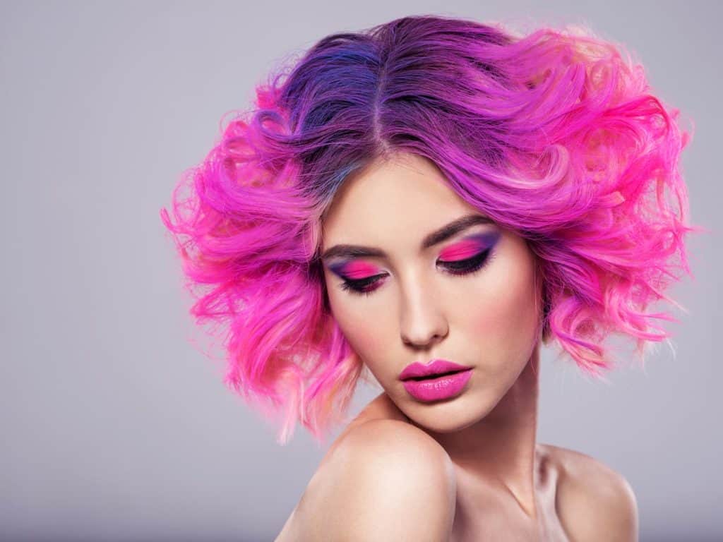 neon pink-colored short curly bob with purple roots