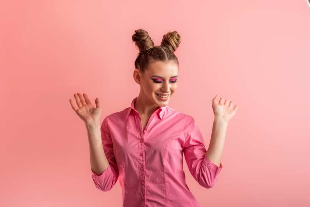 a woman with high space buns hairdo wearing pink top with pink eyeshadow in a pink backdrop