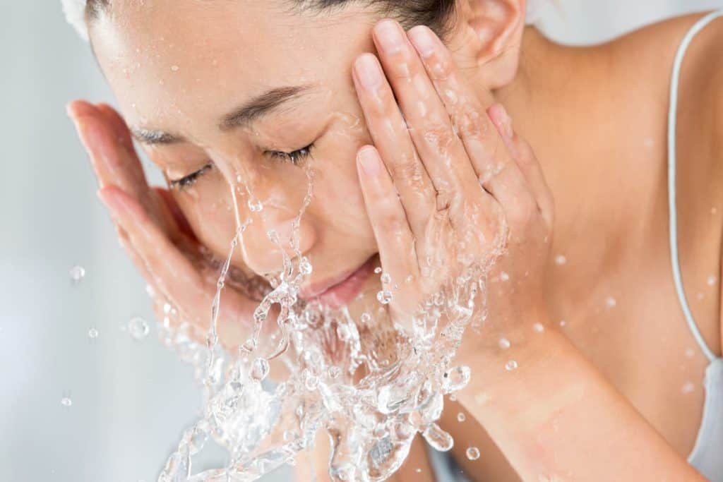 A woman is washing her face with water.