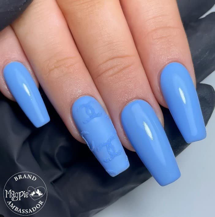A woman's hand is with a blue nail polish and matte accent nail with embossed Chanel imprints