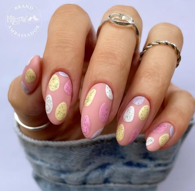 A woman with nails painted in a matte nude polished and multicolored speckled eggs designs
