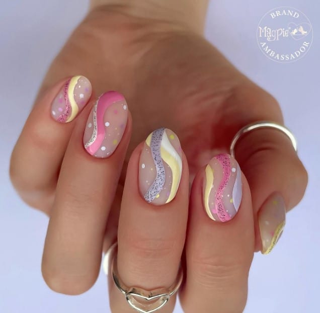 A woman's hand with matte nude nails are made even more gorgeous with pink, yellow, white, and purple dots with swirls designs