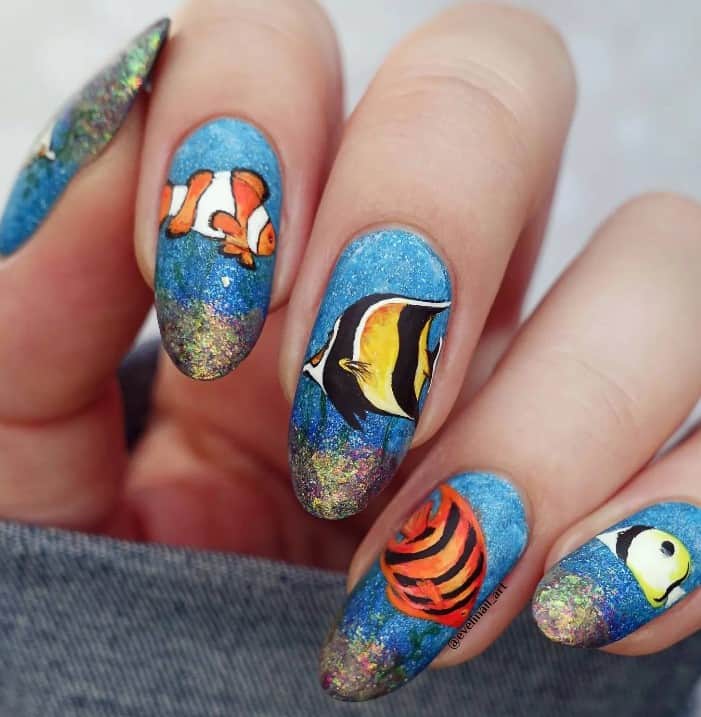 hand-painted tropical fish nail art, glittery blue base, and iridescent flakes at the tips, which recreate life at the bottom of the ocean