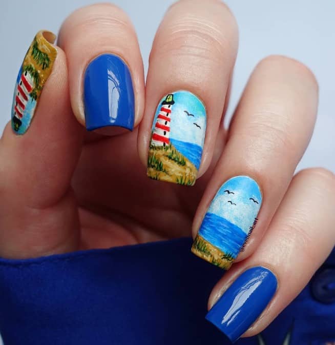 nail art of lighthouses, birds, the ocean, blue skies, and green grass with plain blue accent nails