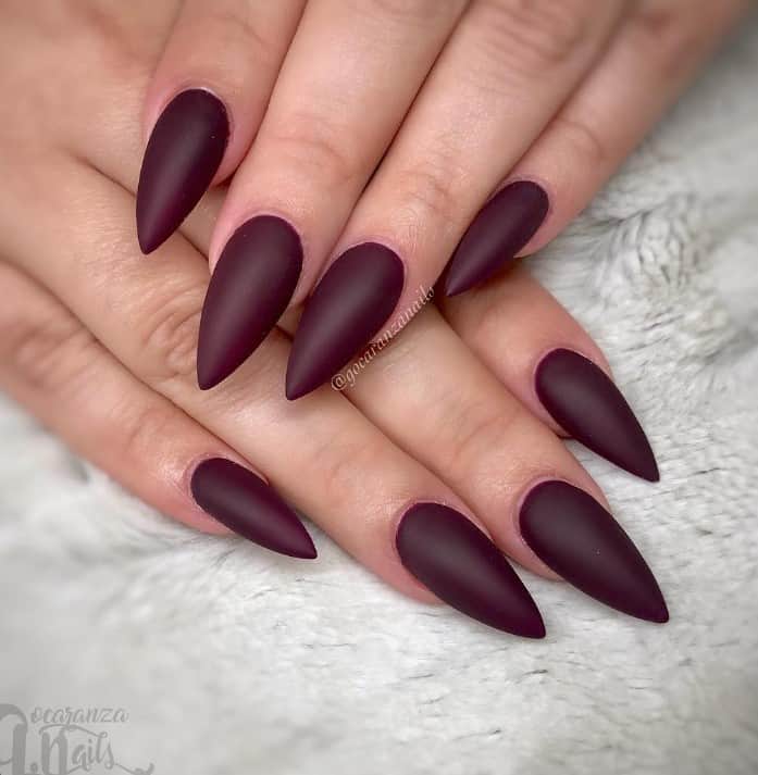 Maroon stiletto nails on a woman's hand.