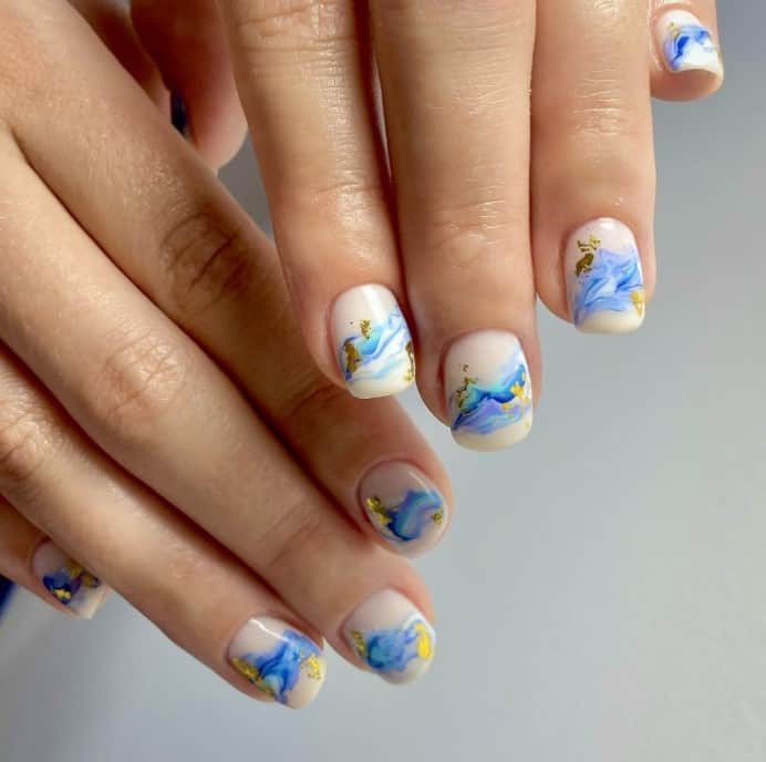 white and blue marble design with wave-like splashes accentuated with gold foil on the middle of creamy white nails