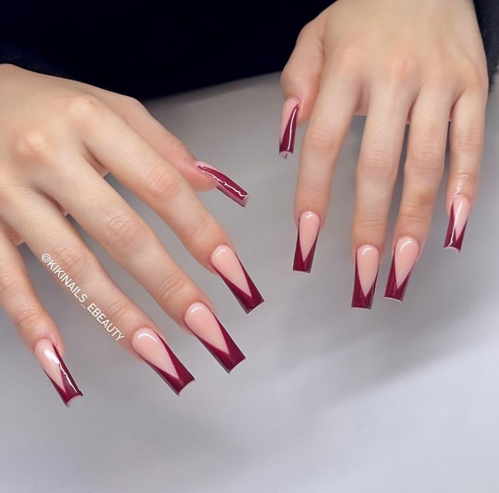 A woman's hands with extra-long square nails in peach, glammed up by glossy burgundy V tips
