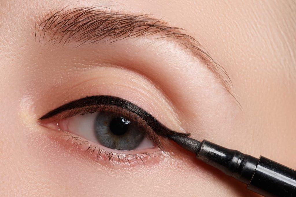 A woman is applying black eyeliner to her eye.