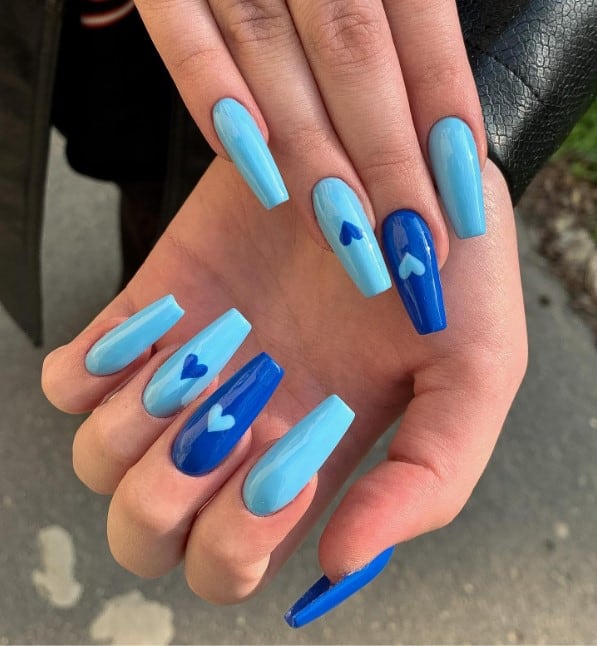 A woman's hand with pale-blue nails with dark blue accents, finished with hearts on accent nails and a glossy