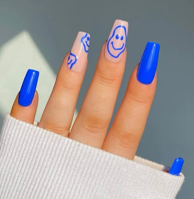 A woman holding a blue nail with a  light nude base with melted smileys that come in various sizes